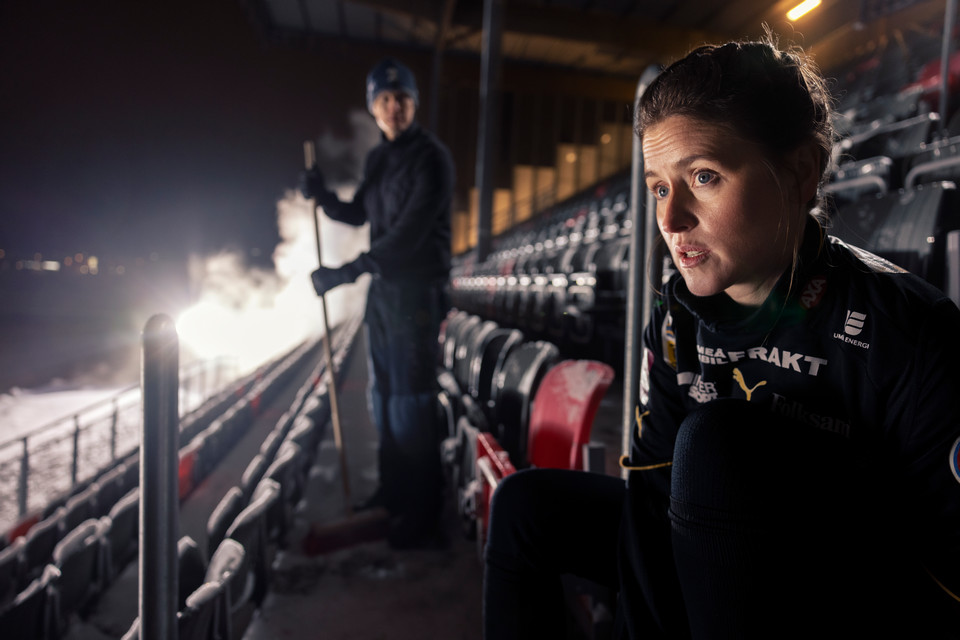 Kvinnlig fotbollsspelare knyter skor på en tom läktare.