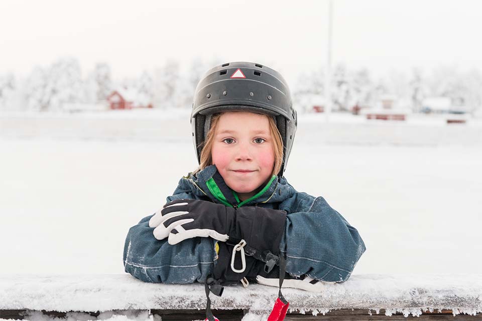 Ett barn med hjälm lutandes mot en rinksarg på vintern.