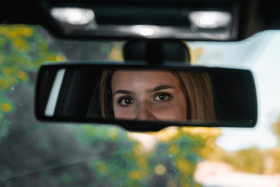 Ung kvinnas spegelbild syns i inre backspegel på bil.