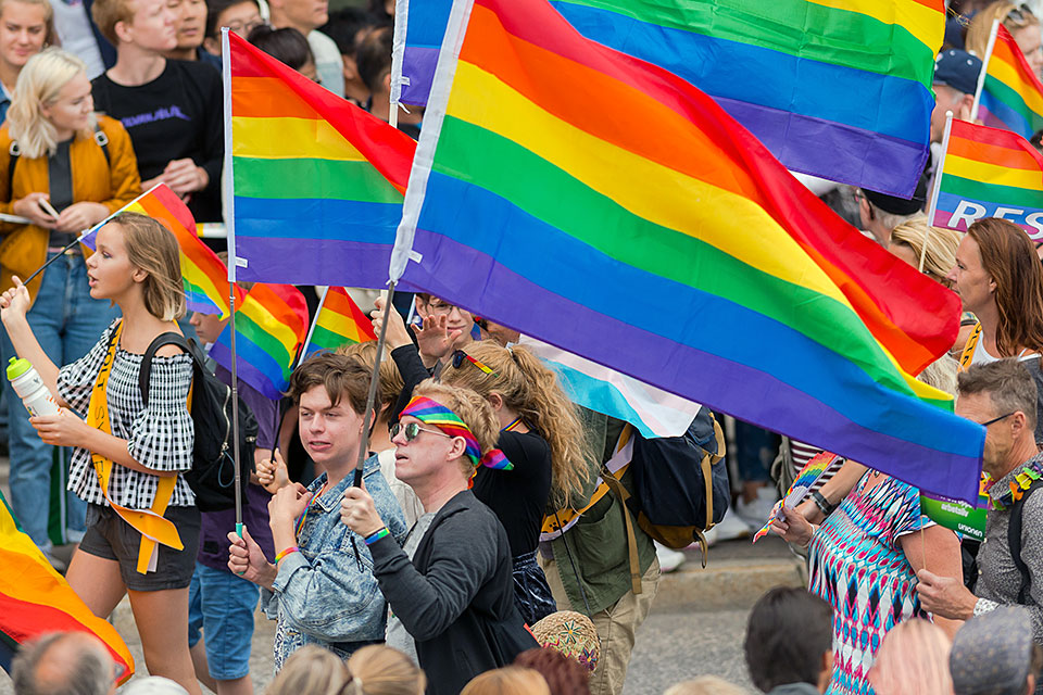 Personer i Pride-tåg med regnbågsflaggor