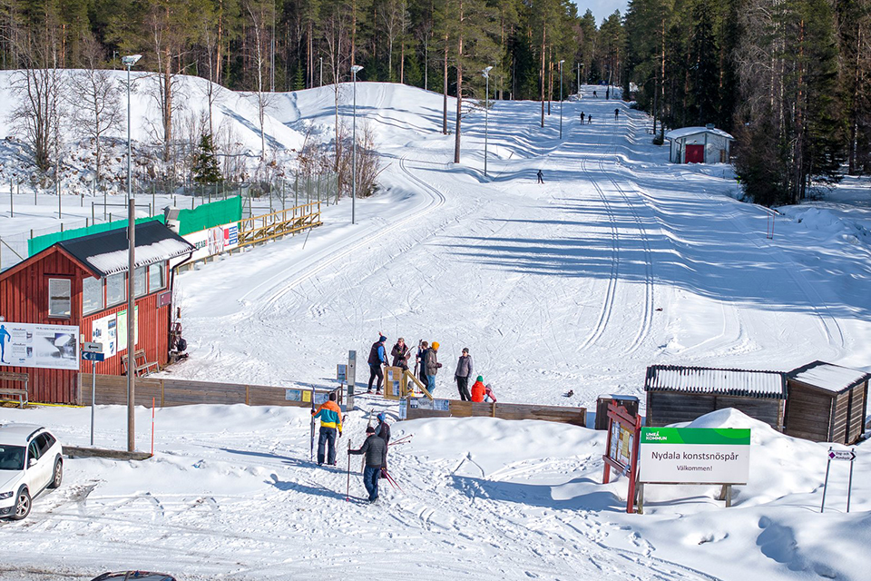 Spårstart på Nydala konstsnöspår. Männsikor på skidor som köar för att få komma in och åka skidor. Mycket snö på backen.