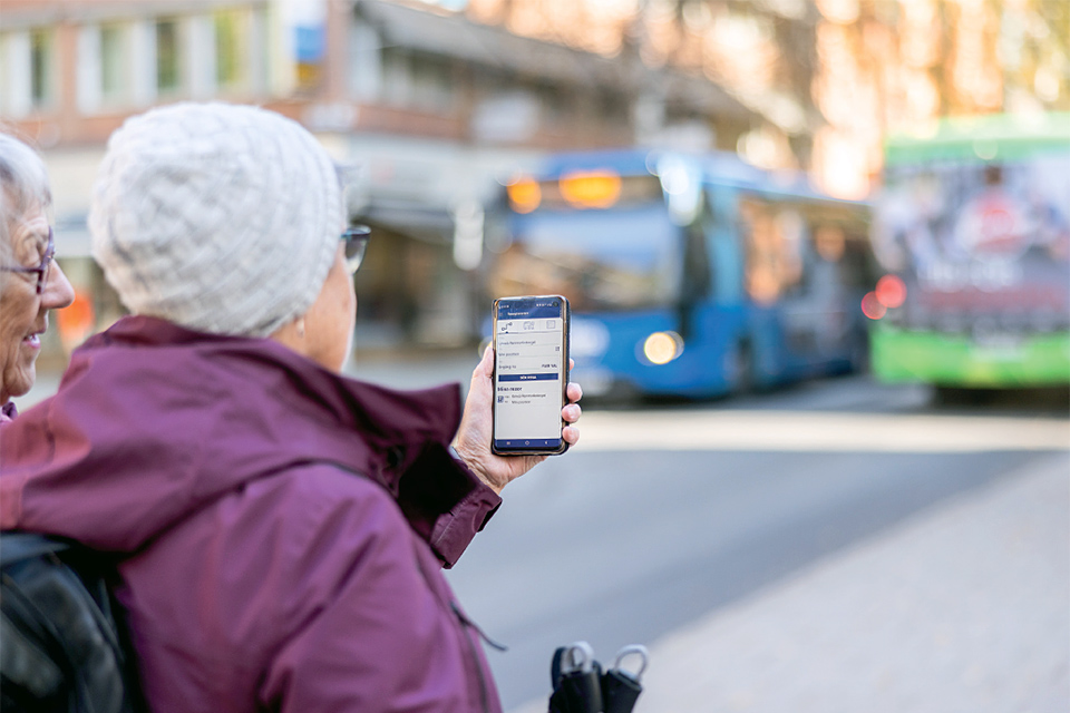 Kvinnor kollar på mobiltelefon, bussar i bakgrunden