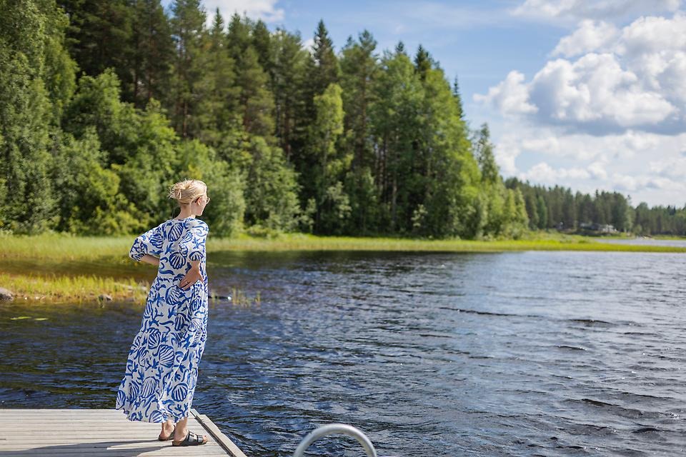 Kvinna står på brygga och ser ut över sjö.