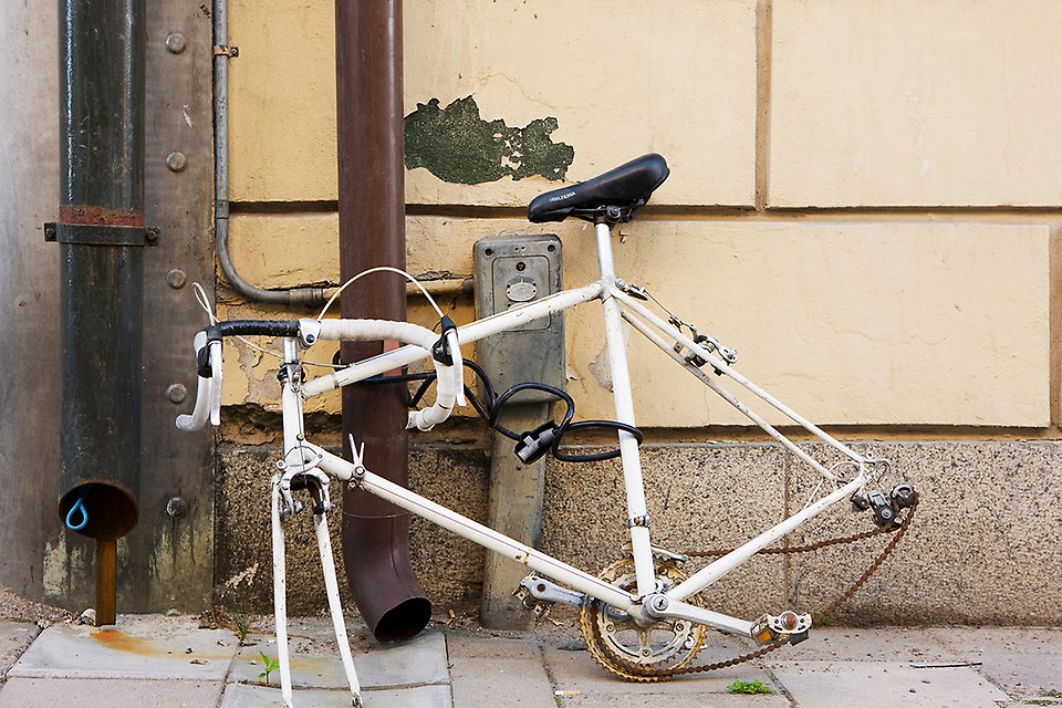 En övergiven och trasig vit cykel, som är fastkedjan vid ett stuprör. 